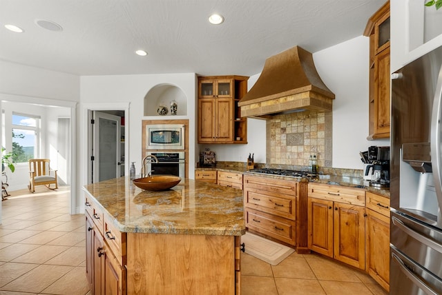 5959 Hayes Creek Rd, Missoula, MT 59804 - kitchen featuring stainless steel appliances, custom exhaust hood, brown cabinetry, light tile patterned floors, and a kitchen island