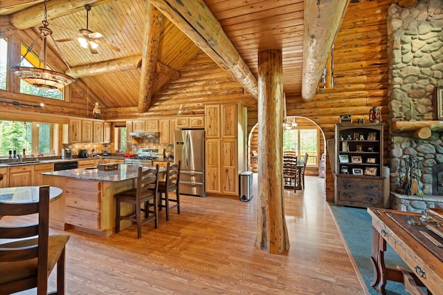 421 Swanson Lodge Rd, Troy, MT 59935 - kitchen with stainless steel appliances, log walls, wooden ceiling with exposed beams, under cabinet range hood, and a kitchen island with sink