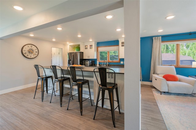 1520 Highland St, Helena, MT 59601 - kitchen featuring stainless steel fridge, light wood-style flooring, white cabinetry, a breakfast bar, and recessed lighting