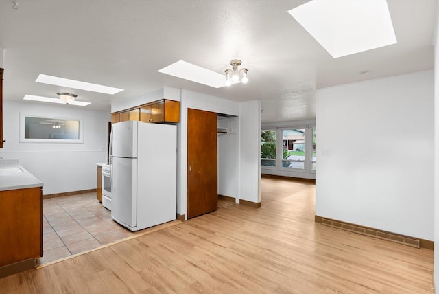 2611 Gilbert Ave, Missoula, MT 59802 - kitchen with white appliances, a skylight, brown cabinetry, and light wood-style flooring
