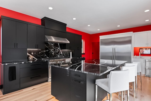 2813 Pine Lakes Ct, Stevensville, MT 59870 - kitchen featuring exhaust hood, dark cabinets, a kitchen island, appliances with stainless steel finishes, and light wood finished floors