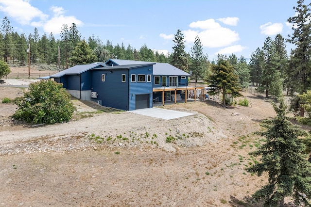 2813 Pine Lakes Ct, Stevensville, MT 59870 - back of property featuring dirt driveway, a garage, a wooden deck, and view of scattered trees