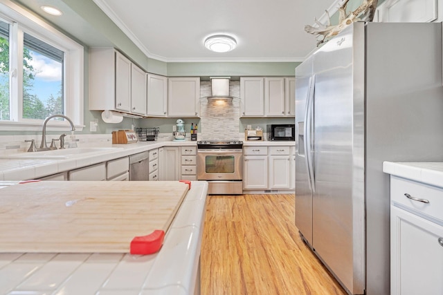 791 Springwood Ln, Kalispell, MT 59901 - kitchen featuring appliances with stainless steel finishes, wall chimney exhaust hood, light wood-style floors, crown molding, and backsplash