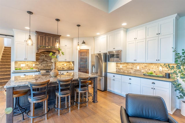 128 Antler Peak Ln, Kalispell, MT 59901 - kitchen featuring stainless steel appliances, light wood-style flooring, decorative backsplash, a breakfast bar area, and recessed lighting