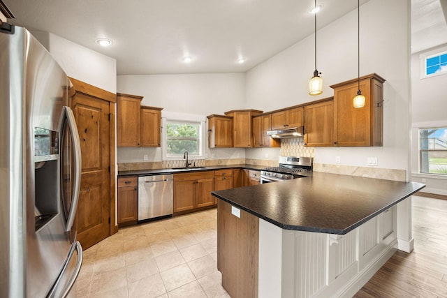 150 Swede Trl, Kalispell, MT 59901 - kitchen featuring appliances with stainless steel finishes, under cabinet range hood, a peninsula, brown cabinets, and high vaulted ceiling