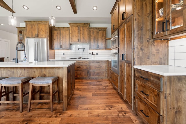 331 Deer Creek Rd, Somers, MT 59932 - kitchen with stainless steel appliances, dark wood-style floors, decorative backsplash, brown cabinets, and a breakfast bar