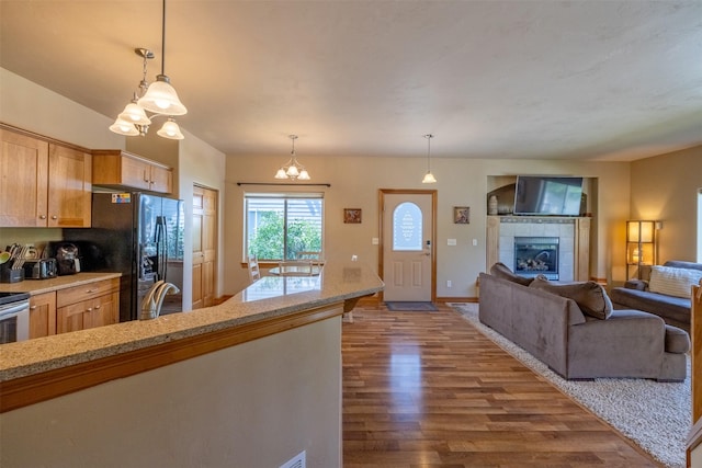 310 Barney St Unit B, Helena, MT 59602 - kitchen featuring black refrigerator with ice dispenser, wood finished floors, a tile fireplace, light stone counters, and open floor plan