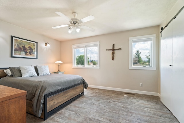 3782 E Riggs St, East Helena, MT 59635 - bedroom featuring a barn door, multiple windows, wood finished floors, and ceiling fan