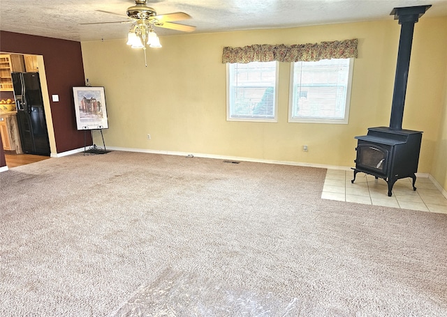 1109 W Main St, Hamilton, MT 59840 - unfurnished living room featuring light colored carpet, a wood stove, ceiling fan, a textured ceiling, and light tile patterned floors