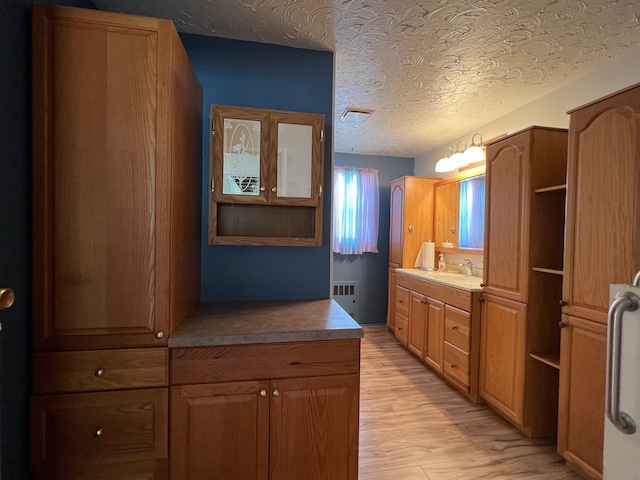 214 Church St, Thompson Falls, MT 59873 - kitchen featuring radiator heating unit, open shelves, light wood-style flooring, a textured ceiling, and brown cabinetry
