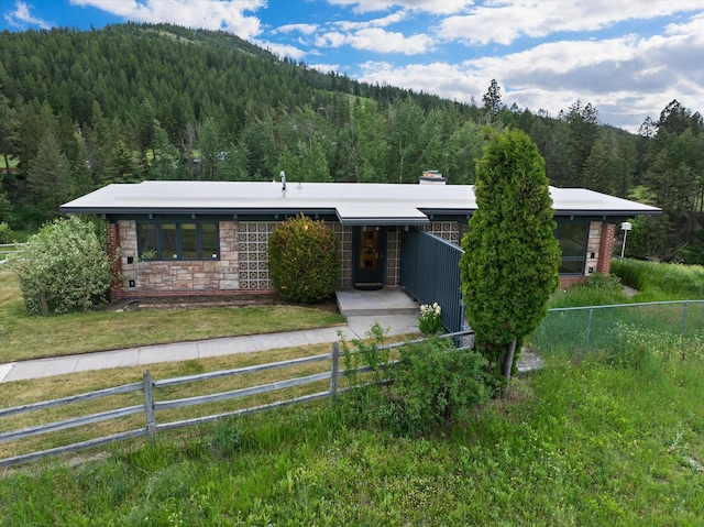 1695 Whalebone Dr, Kalispell, MT 59901 - ranch-style home with a wooded view, a fenced front yard, stone siding, and a chimney