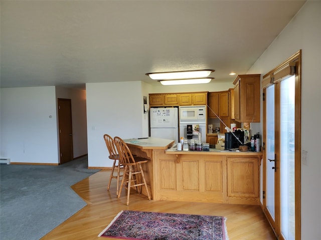 650 Hollibaugh Rd, Stevensville, MT 59870 - kitchen with white appliances, a peninsula, light wood-style floors, a kitchen bar, and a baseboard radiator
