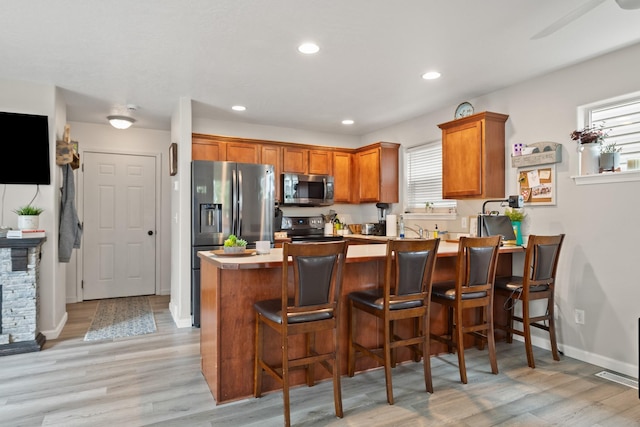 2331 W Sussex Ave, Missoula, MT 59801 - kitchen featuring stainless steel appliances, a peninsula, brown cabinetry, light wood-style floors, and a kitchen bar