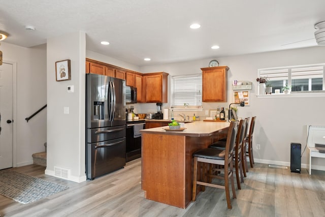 2331 W Sussex Ave, Missoula, MT 59801 - kitchen featuring stainless steel appliances, a peninsula, light wood finished floors, brown cabinetry, and a breakfast bar