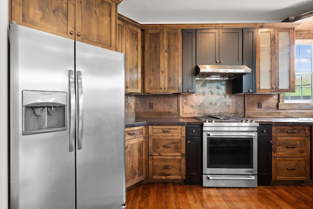 54 Bluebird Dr, Kalispell, MT 59901 - kitchen featuring stainless steel appliances, under cabinet range hood, dark countertops, tasteful backsplash, and dark wood-style flooring