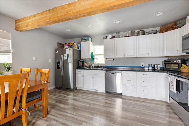 3265 US Highway 2 W, Kalispell, MT 59901 - kitchen with appliances with stainless steel finishes, dark countertops, white cabinets, light wood-style floors, and beam ceiling