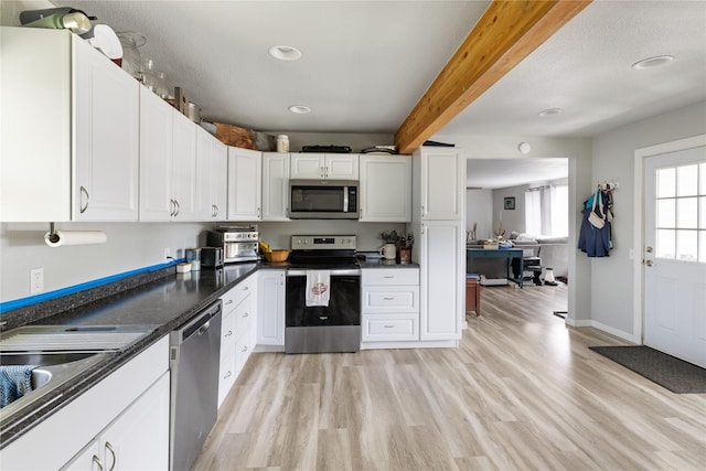 3265 US Highway 2 W, Kalispell, MT 59901 - kitchen featuring appliances with stainless steel finishes, dark countertops, light wood-type flooring, white cabinets, and beam ceiling