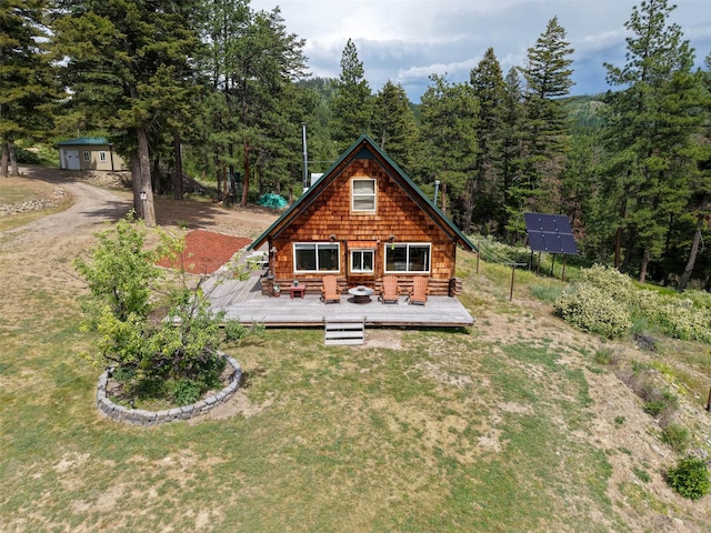 18998 Oris Ln, Florence, MT 59833 - rear view of house with solar panels, a wooden deck, a view of trees, a yard, and an outdoor hangout area