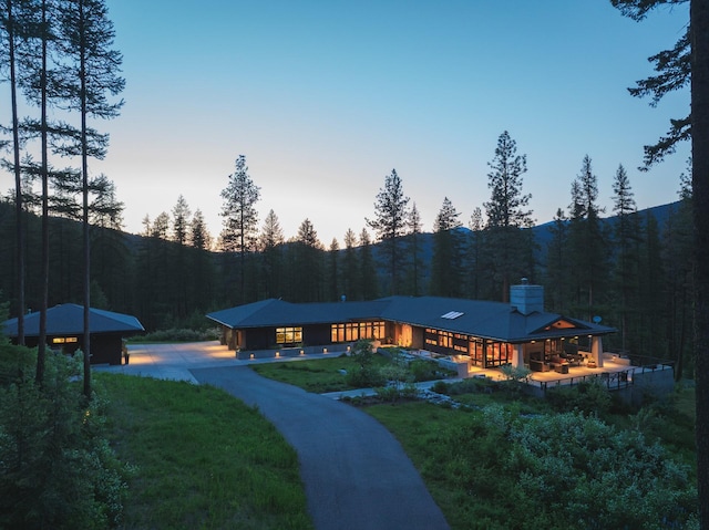 6601 Russian Joe Rd, Missoula, MT 59802 - back of property at dusk with a chimney, a wooded view, a yard, and a mountain view