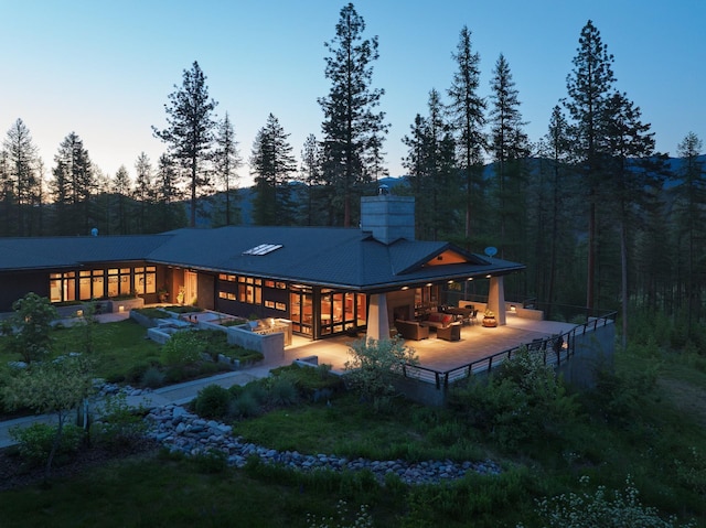 6601 Russian Joe Rd, Missoula, MT 59802 - back of house at dusk with outdoor lounge area, a chimney, a view of trees, and a metal roof