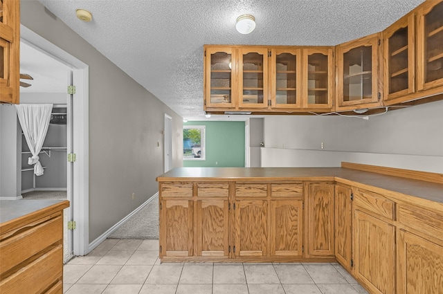 1312 2nd Ave NW, Great Falls, MT 59404 - kitchen with a textured ceiling, glass insert cabinets, a peninsula, light tile patterned flooring, and brown cabinets