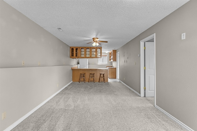 1312 2nd Ave NW, Great Falls, MT 59404 - kitchen featuring a peninsula, a ceiling fan, brown cabinets, a textured ceiling, and a kitchen bar