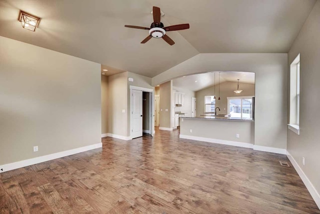 2909 Travis Ave, Helena, MT 59601 - unfurnished living room featuring ceiling fan, vaulted ceiling, wood finished floors, and arched walkways