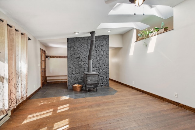 28578 Wapiti Ln, Bigfork, MT 59911 - unfurnished living room featuring a wood stove, wood finished floors, a baseboard radiator, a ceiling fan, and a skylight