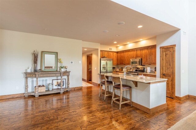 6008 St Moritz Dr Unit K, Whitefish, MT 59937 - kitchen featuring stainless steel appliances, a center island with sink, light stone counters, dark wood finished floors, and brown cabinetry