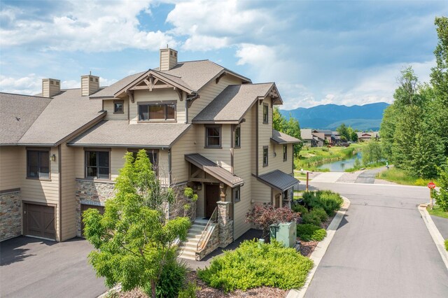 6008 St Moritz Dr Unit K, Whitefish, MT 59937 - view of front of house with a chimney, roof with shingles, an attached garage, stone siding, and a water and mountain view