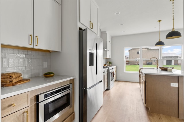 5465 Remington Dr, Missoula, MT 59808 - kitchen with appliances with stainless steel finishes, light wood-style floors, decorative backsplash, pendant lighting, and white cabinetry
