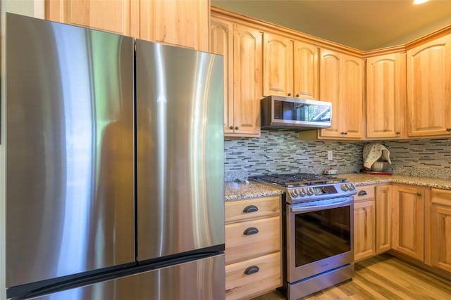 10487 Coulter Pine St, Lolo, MT 59847 - kitchen featuring appliances with stainless steel finishes, light brown cabinetry, light stone countertops, tasteful backsplash, and light wood-style flooring
