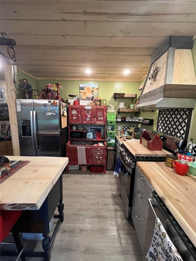 27687 Yaak River Rd, Troy, MT 59935 - kitchen featuring black range oven, dishwashing machine, stainless steel fridge, butcher block counters, and custom range hood