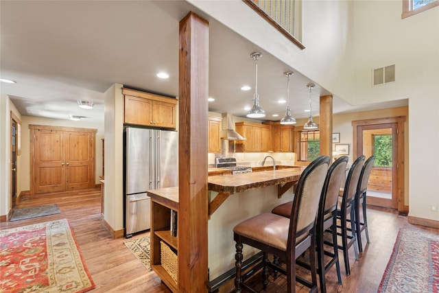 220 Cliff Creek Rd, Whitefish, MT 59937 - kitchen with stainless steel appliances, wall chimney range hood, a breakfast bar area, butcher block countertops, and light wood-style flooring