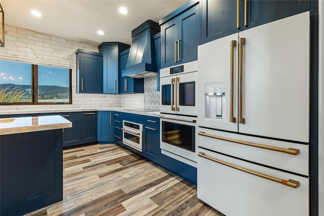 60951 Sparky Dr, Saint Ignatius, MT 59865 - kitchen with white appliances, blue cabinetry, custom range hood, light countertops, and light wood finished floors