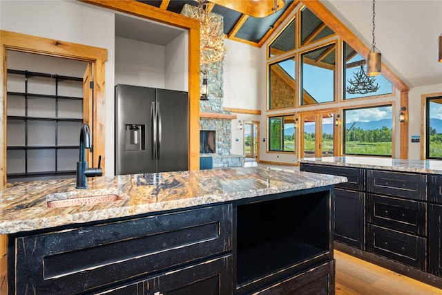 600 Ringneck Dr, Kalispell, MT 59901 - kitchen featuring stainless steel fridge with ice dispenser, dark cabinets, light wood finished floors, light stone counters, and vaulted ceiling