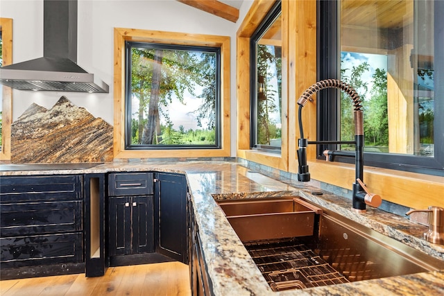 600 Ringneck Dr, Kalispell, MT 59901 - kitchen with wall chimney range hood, black electric cooktop, light stone counters, lofted ceiling, and dark cabinets