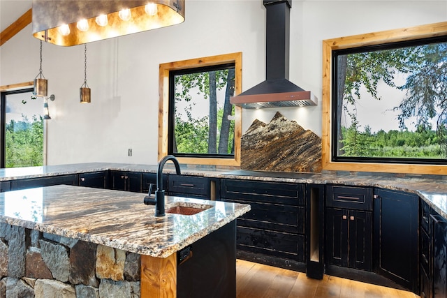 600 Ringneck Dr, Kalispell, MT 59901 - kitchen with wall chimney range hood, light stone counters, light wood finished floors, and dark cabinets