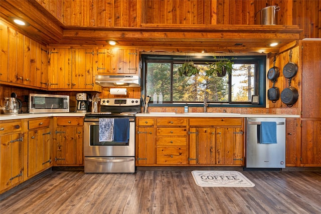 630 Tally Lake Rd, Whitefish, MT 59937 - kitchen featuring stainless steel appliances, under cabinet range hood, light countertops, wooden walls, and brown cabinets