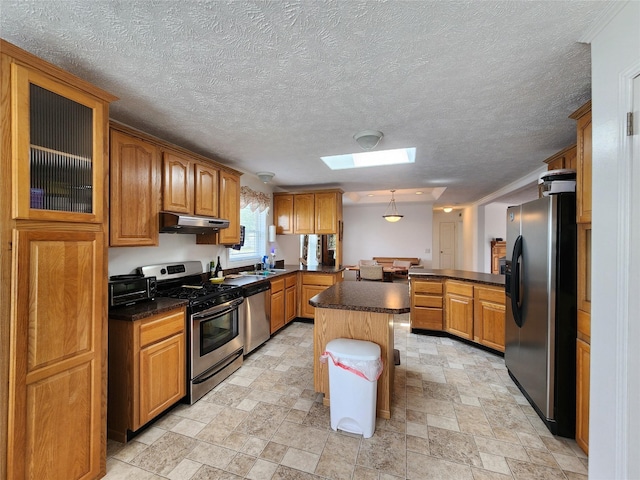 1208 8th Ave NW, Great Falls, MT 59404 - kitchen featuring appliances with stainless steel finishes, under cabinet range hood, a peninsula, a skylight, and brown cabinetry