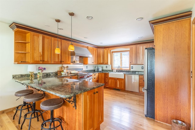 2755 US Highway 93 W, Whitefish, MT 59937 - kitchen with appliances with stainless steel finishes, a peninsula, wall chimney exhaust hood, brown cabinets, and light wood-type flooring