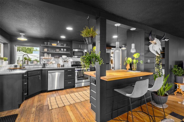 438 Somers Ave, Whitefish, MT 59937 - kitchen with appliances with stainless steel finishes, butcher block countertops, a kitchen bar, light wood-type flooring, and a textured ceiling