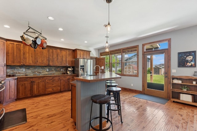 101 Heavens Peak Dr, Kalispell, MT 59901 - kitchen with stainless steel fridge with ice dispenser, light wood-style flooring, a kitchen bar, decorative backsplash, and brown cabinets