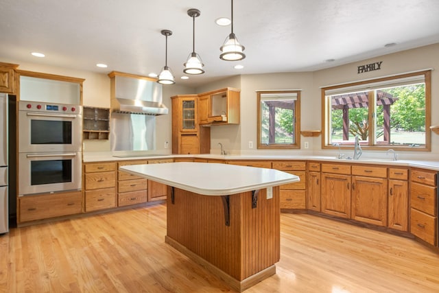 9995 Obrien Creek Rd, Missoula, MT 59804 - kitchen featuring stainless steel appliances, wall chimney range hood, light countertops, a center island, and light wood-style floors