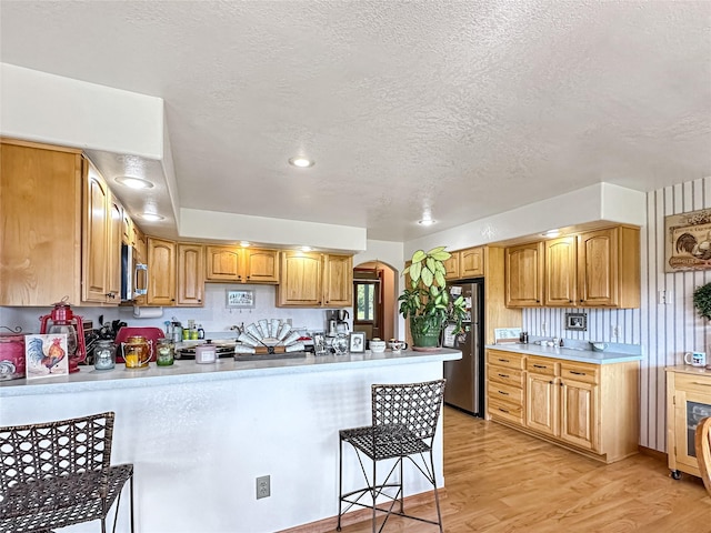 2 Hardy Cir, Ennis, MT 59729 - kitchen with a peninsula, arched walkways, stainless steel appliances, a breakfast bar, and light wood-style floors