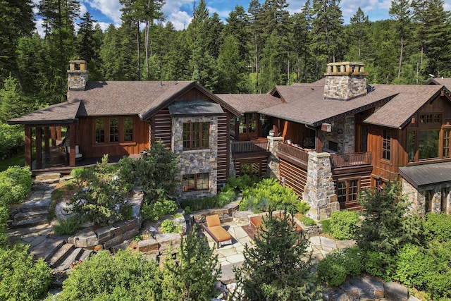 1263 Spencer Ridge Rd, Whitefish, MT 59937 - view of front facade featuring a chimney, stone siding, a patio area, and roof with shingles