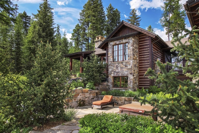 1263 Spencer Ridge Rd, Whitefish, MT 59937 - view of side of property featuring stone siding, a patio, and a chimney