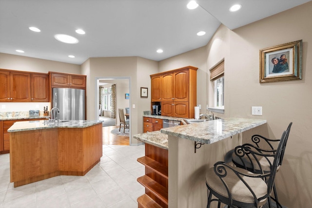 18 Buffalo Hill Cir, Kalispell, MT 59901 - kitchen featuring stainless steel appliances, a peninsula, light stone countertops, brown cabinetry, and a breakfast bar