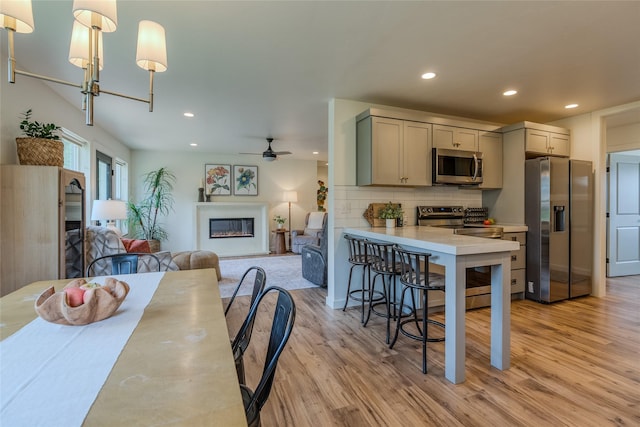 405 Kendal Loop, Kalispell, MT 59901 - kitchen with appliances with stainless steel finishes, a breakfast bar, light wood finished floors, a glass covered fireplace, and decorative backsplash