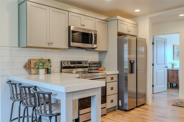 405 Kendal Loop, Kalispell, MT 59901 - kitchen featuring stainless steel appliances, light countertops, backsplash, a kitchen bar, and light wood finished floors